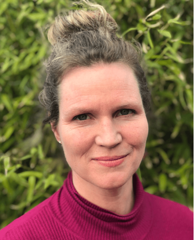 A portrait image of a woman with her hair tied up in a bun and wearing a pink turtle neck top.