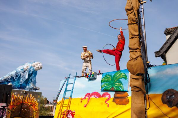 An image of two circus performers on top of a mural with a blue sky background.