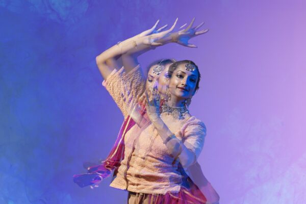 An image of an a South Asian female dancer dancing against a purple background.