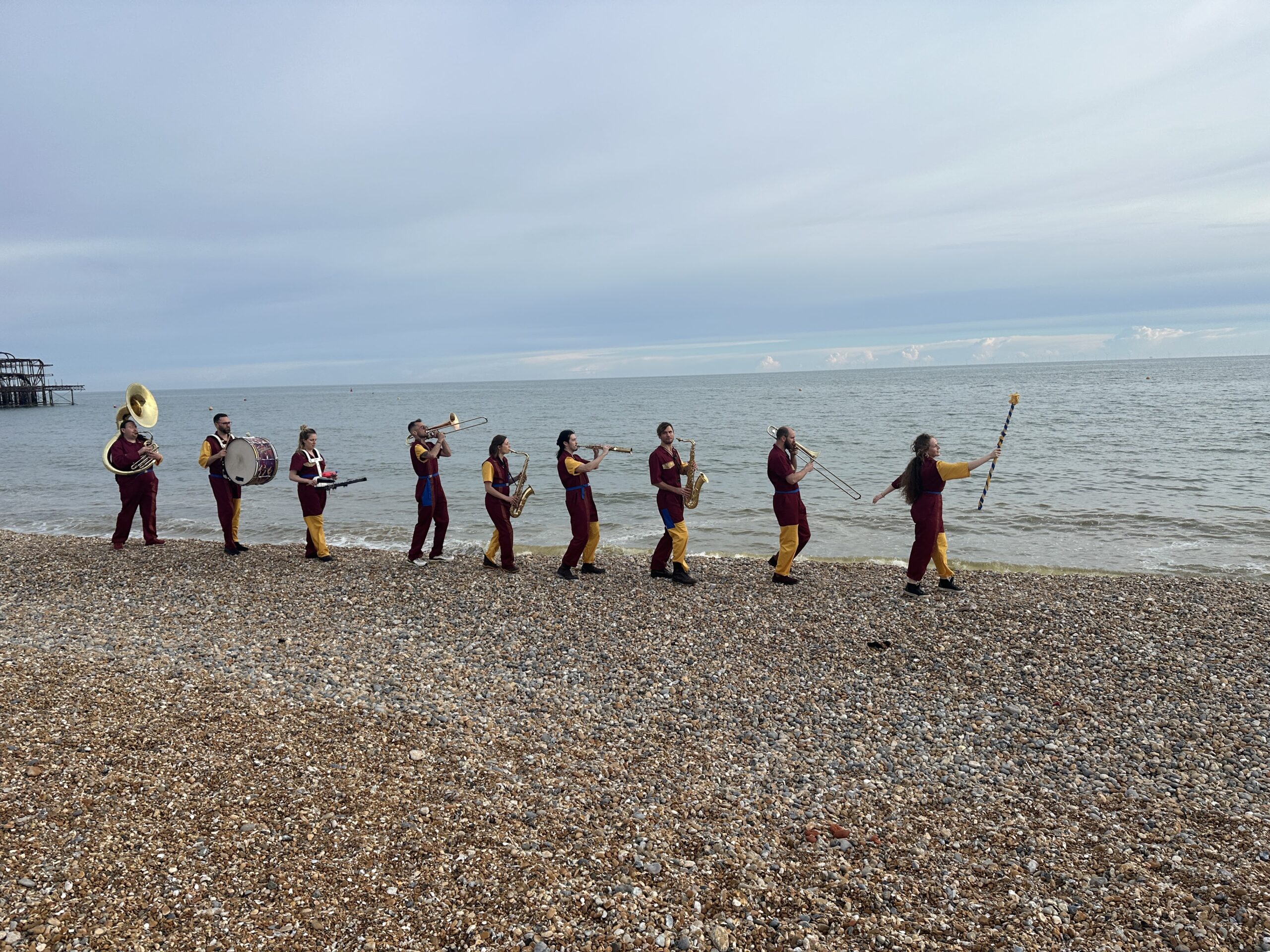 An image of a marching band walking along the beach and playing various brass and percussion instruments.