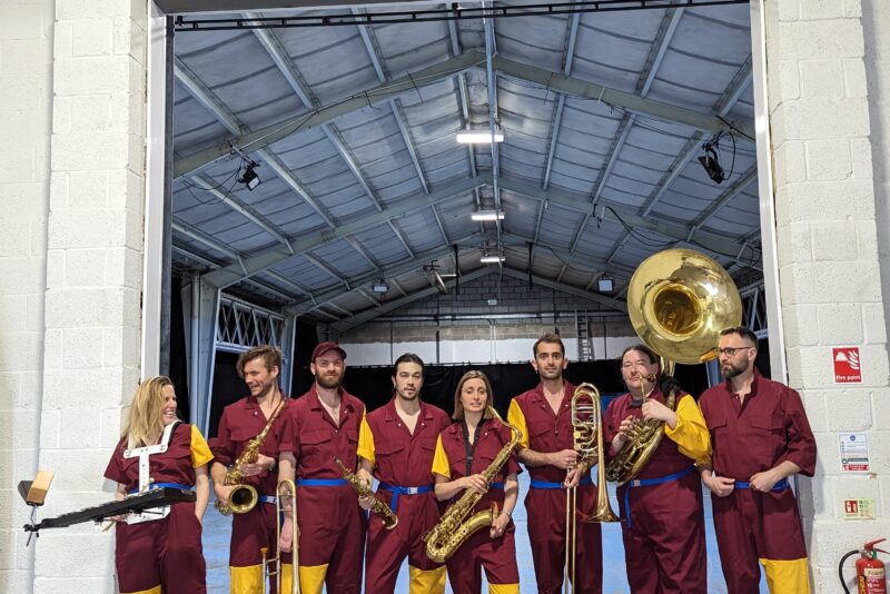 An image of a marching band stood in front of a large doorway.