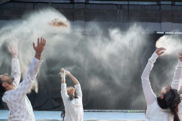 An image of a group of performers wearing white while throwing sand into the air.