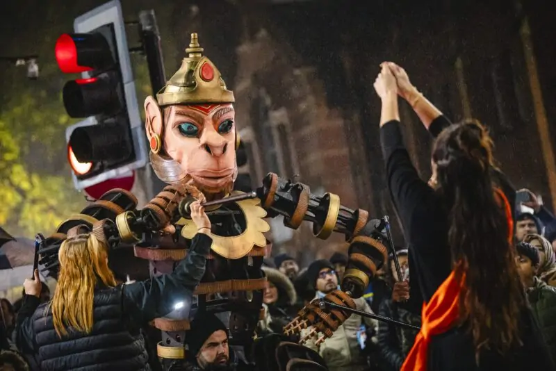 An image of a life sized puppet with a traffic light behind it and a female with her back to the camera in front with her arms outstretched and back to the camera.