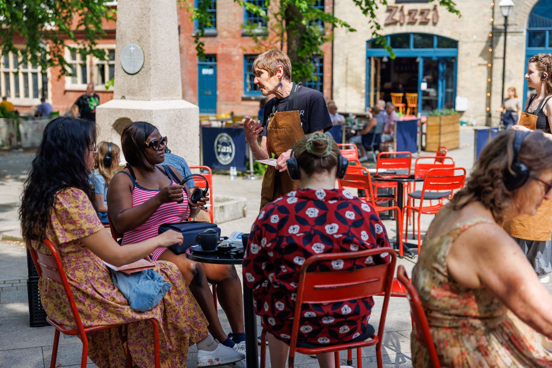 An image of a group of people sat around a table with a man stood speaking to them.