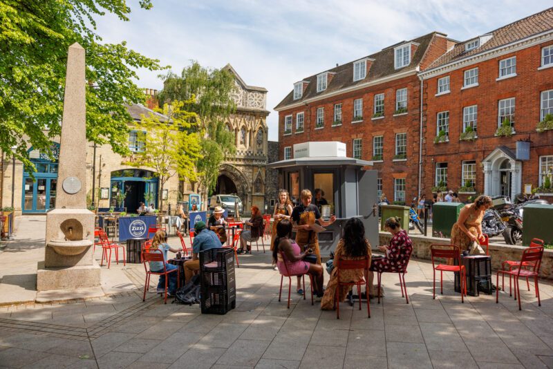 An image of a crowd in a city square sat on some chairs