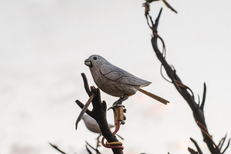 An image of wooden white birds perched on tree branches with a cloudy sky background.