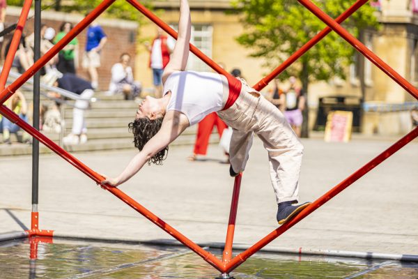 An image of a female dancer suspended on a cube shaped frame.