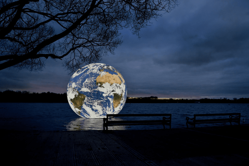 An image of a spherical earth floating on a lake at dusk