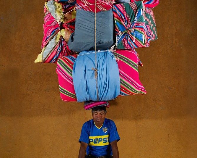 An image of a man sat down with multiple bales of bedding balancing on top of his head.