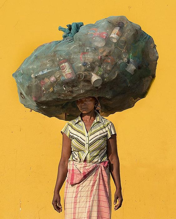 An image of a woman balancing a large bag on her head filled with rubbish.