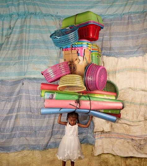 An image of a little girl with multiple colourful baskets and rolled up tubes balancing on her head.
