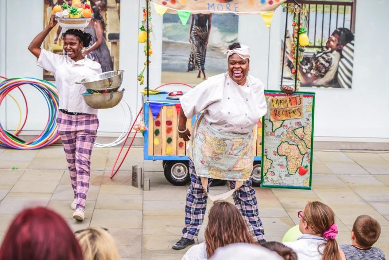 An image of two women wearing chef's uniform dancing in from of a makeshift kitchen.