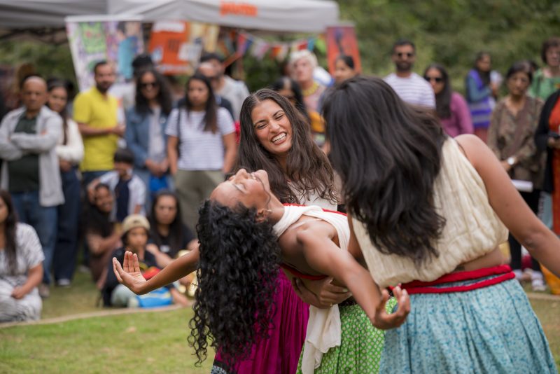 An image of three female dancers with a background audience.