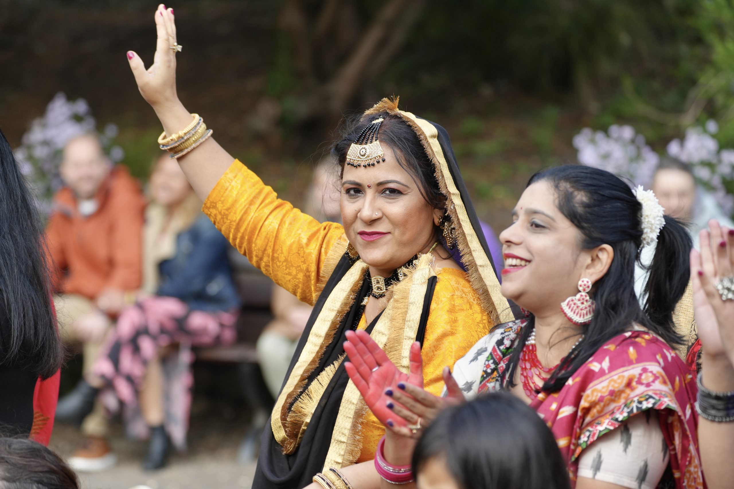 An image of two women dressed in South East Asian traditional clothing. One of them has her hand raised in the air.