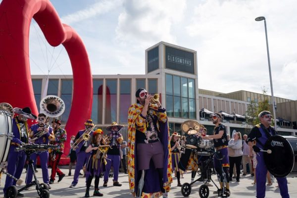 An image of a brass band performing in a town centre square in front of a giant red heart.