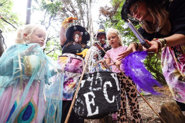 An image of a group of children and an adult female stood around a small stick structure in a wood.