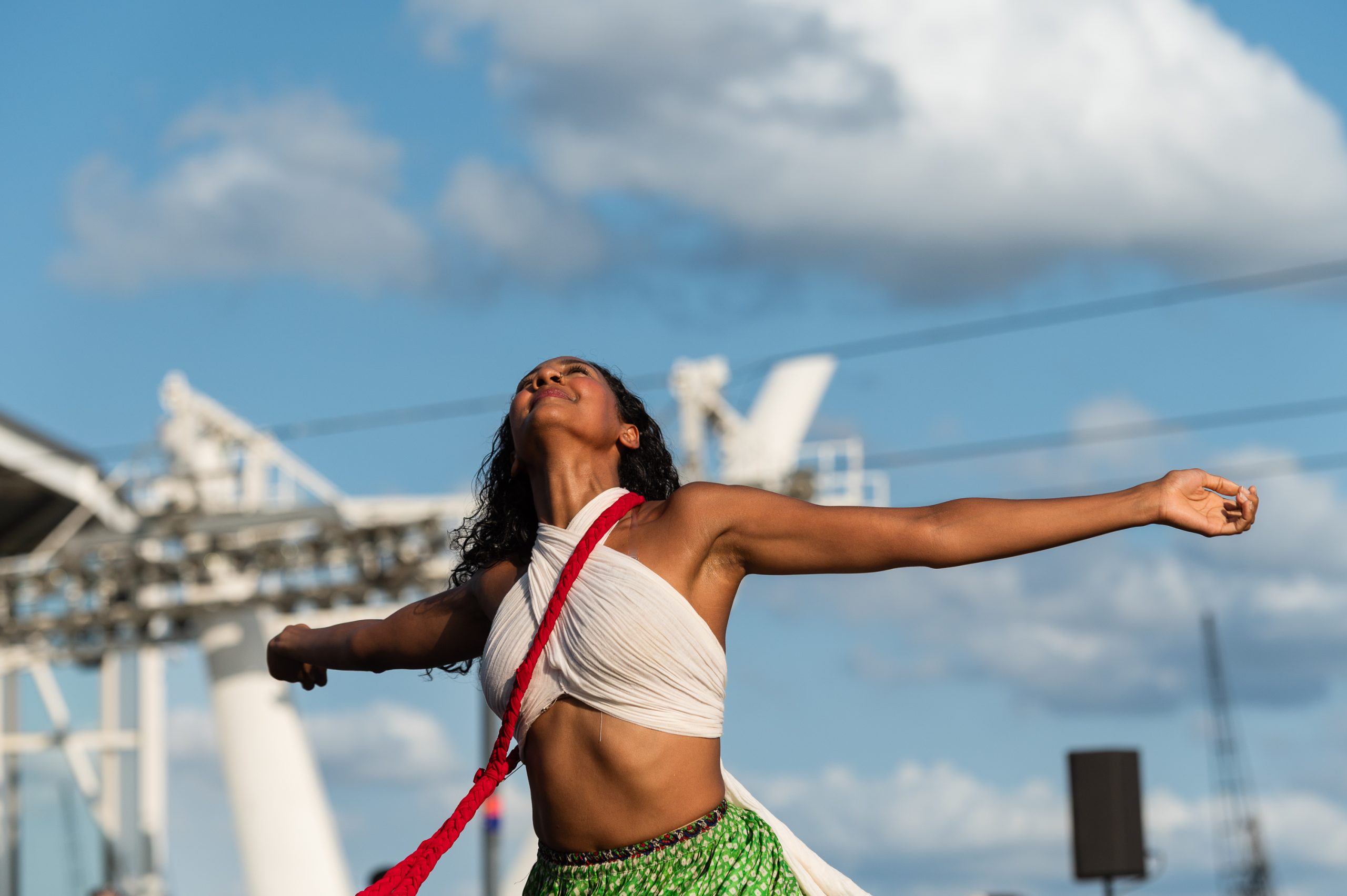 An image of a female dancer with her arms outstretched wearing traditional Indian dress against a blue sky background.